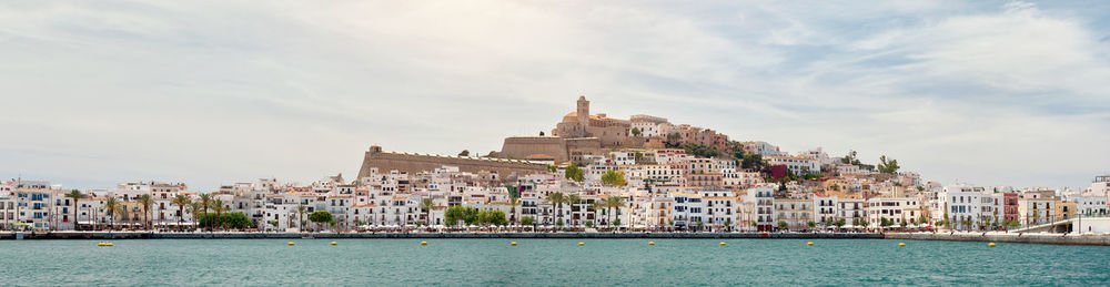 View of buildings at waterfront against cloudy sky