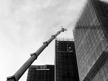 Low angle view of crane by building against sky