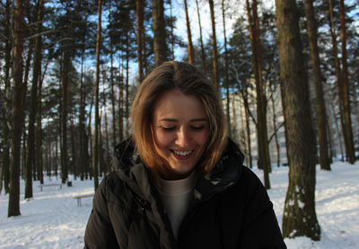 Smiling young woman in forest during winter