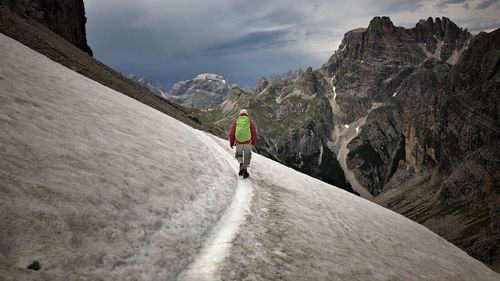 Rear view of man walking on snow covered mountain against sky