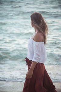 Young woman standing at beach against sky