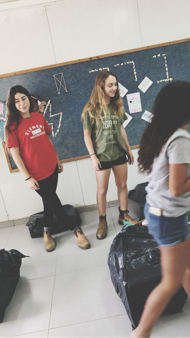 FULL LENGTH OF SMILING YOUNG WOMAN STANDING IN CORRIDOR