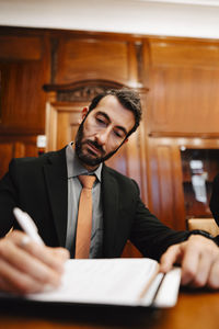 Confident businessman signing contract document sitting at conference table in board room during meeting