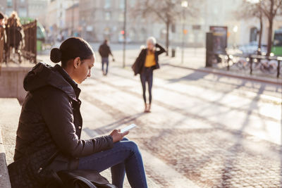 Teenage girl using mobile phone while sitting on steps in city