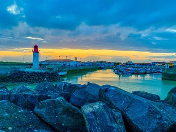 Lighthouse by sea against sky during sunset