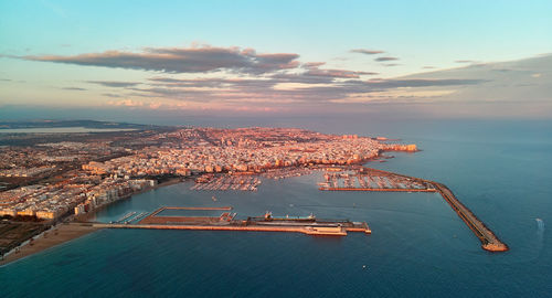 Aerial view of city by sea against sky during sunset