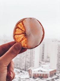 Close-up of hand holding citrus fruit slice with soap sud against buildings