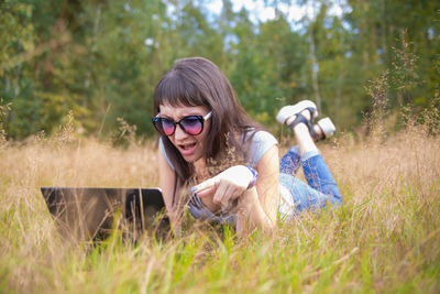 Portrait of young woman holding sunglasses on field