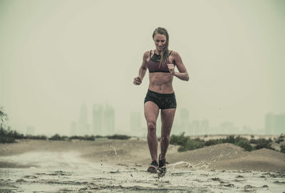 Full length of young woman running in mud against sky