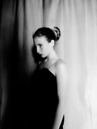 Young woman looking away while standing against curtain at home