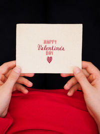 Child in a red sweater holding a handmade postcard with embroidery happy valentine's day.