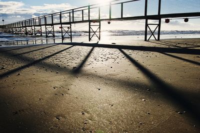 Shadow of railing on beach against sky
