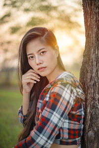 Portrait of beautiful young woman against tree trunk