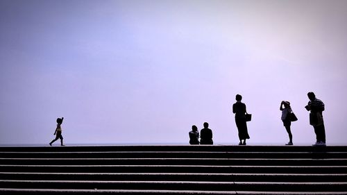 Silhouette people on steps against clear sky