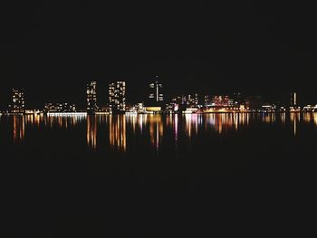 Illuminated cityscape by river against clear sky at night