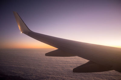 Airplane wing against sky during sunset