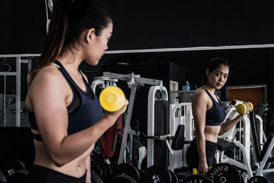 Woman lifting dumbbell with her reflection in mirror at gym