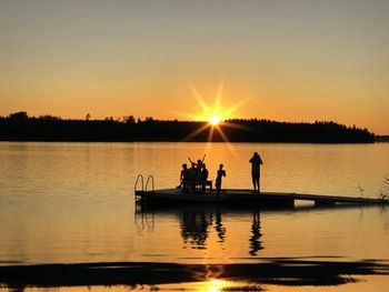 Silhouette people on lake against sky during sunset