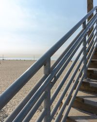 Metal railing on beach against sky