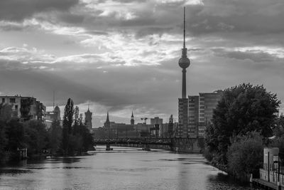 View of buildings by river against cloudy sky