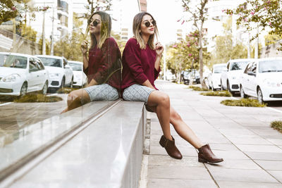 Young woman sitting on sidewalk by reflection glass building