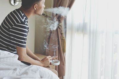 Man smoking cigarette while relaxing on bed