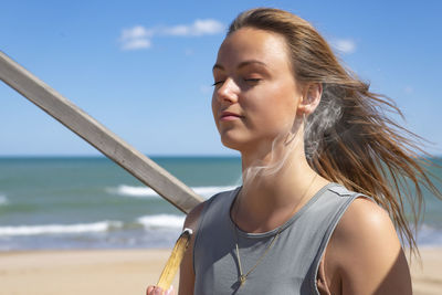 Side view of young woman standing at beach against sky