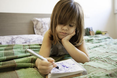 Cute girl writing in diary while lying on bed