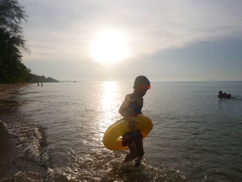 Boy on beach against sky during sunset