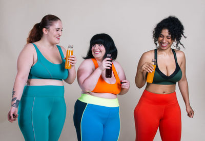 Smiling friends holding drink against colored background