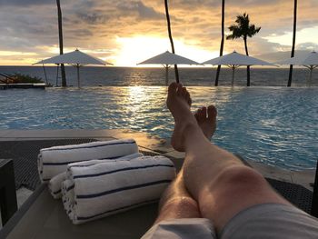 Low section of man relaxing at poolside by sea against cloudy sky