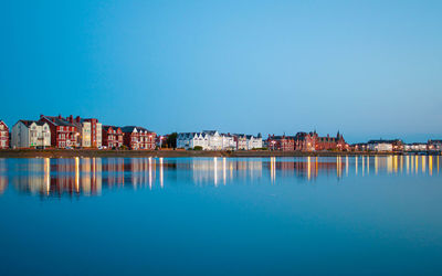 Buildings by lake against blue sky