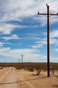 Electricity pylon on dirt road against sky