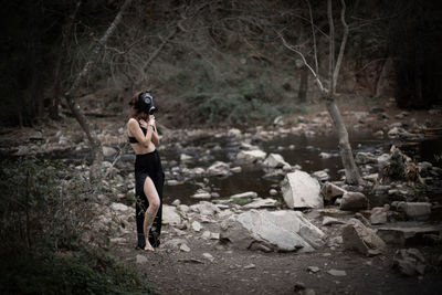 Side view of woman wearing gas mask while covering chest in forest