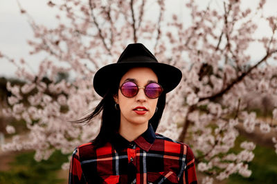 Portrait of woman wearing sunglasses and hat against pink flowers