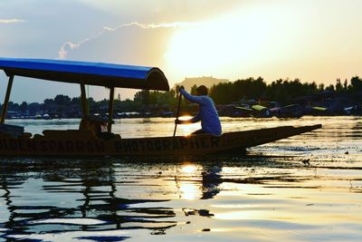 Man on boat in lake against sky during sunset