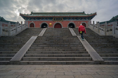 Rear view of man walking towards temple against cloudy sky