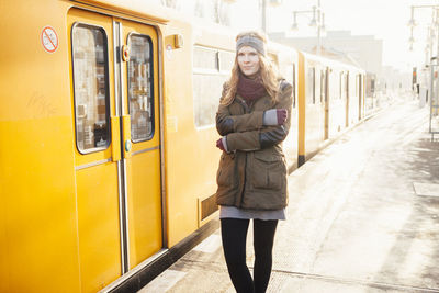 Portrait of beautiful young woman standing by yellow train during winter