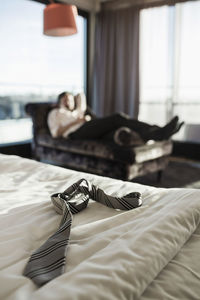 Necktie on hotel bed with businessman resting in background