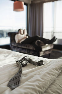 Necktie on hotel bed with businessman resting in background