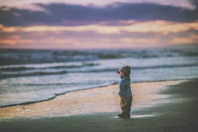 Side view of boy standing on calm beach
