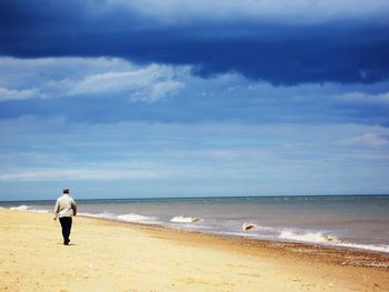 Rear view of man walking at beach against cloudy sky