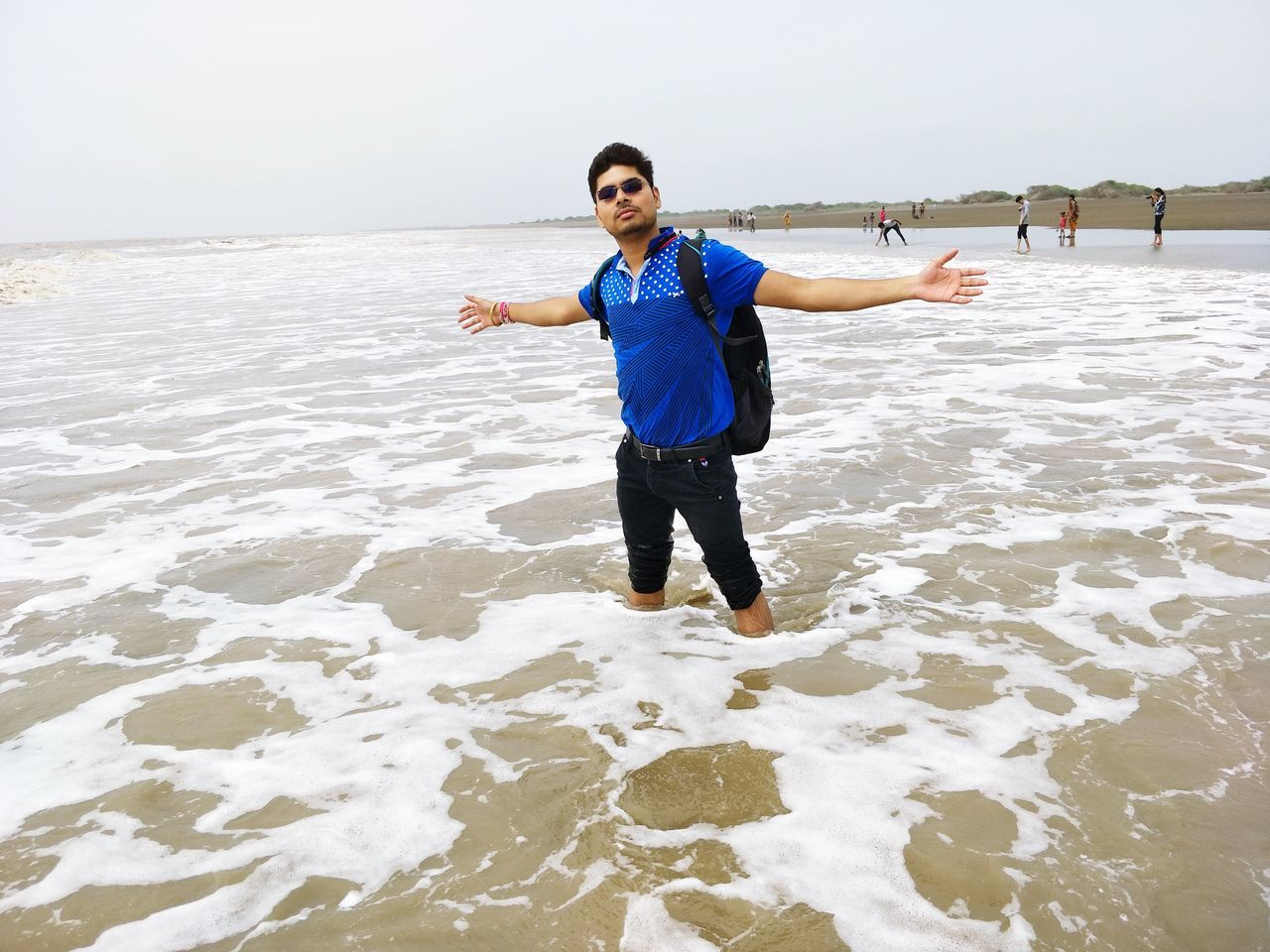 real people, looking at camera, standing, water, one person, front view, portrait, happiness, lifestyles, gesturing, day, leisure activity, nature, sea, arms outstretched, smiling, outdoors, full length, beach, beauty in nature, scenics, young adult, sky, ankle deep in water