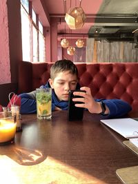 A boy with a a phone sitting in restaurant drinking cocktail