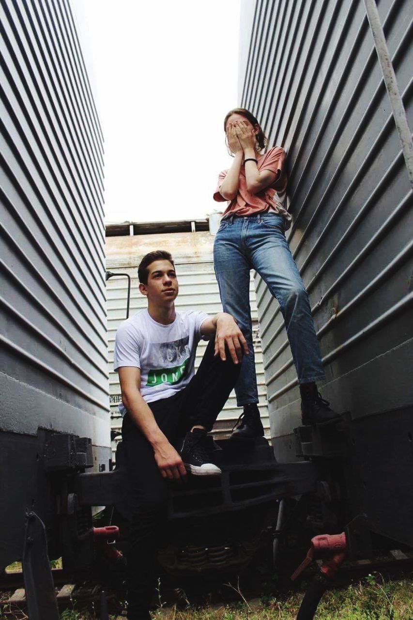 young adult, real people, casual clothing, young men, full length, two people, looking at camera, front view, standing, togetherness, day, portrait, young women, outdoors, architecture, corrugated iron