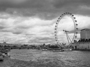 Ferris wheel in city against cloudy sky