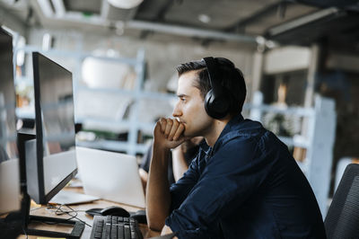 Side view of young programmer with hand on chin sitting and looking at computer in office