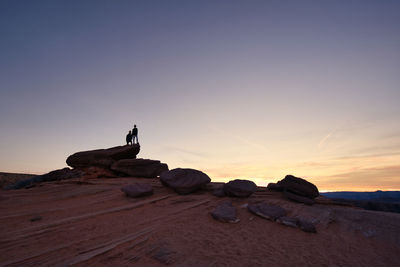 Man on rock against sky during sunset