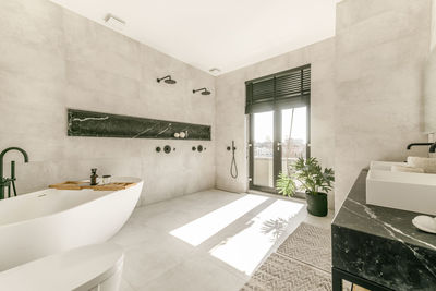 Modern interior of bathroom with white bathtub and ceramic wall mounted toilet and double sinks in minimal style