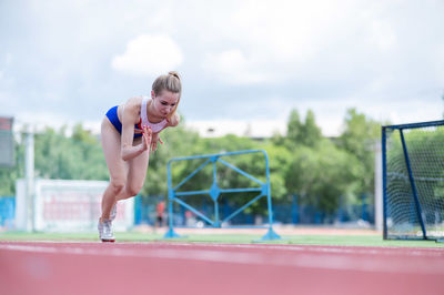 Full length of young woman exercising on field